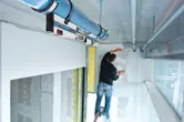 Uma pessoa numa escada a marcar uma parede usando um inclinómetro digital para alinhamento.