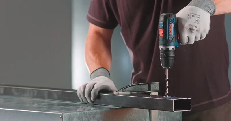 Uma pessoa que utilize equipamento de segurança perfura uma viga metálica com um adaptador FlexiClick.