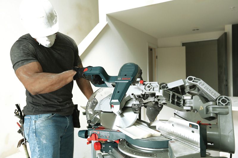 Uma pessoa que utiliza equipamento de segurança ajusta uma serra de esquadria numa sala em construção.