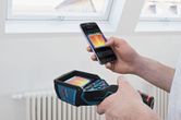 Uma pessoa utiliza uma câmara térmica e um smartphone para visualizar uma imagem térmica em ambientes interiores.