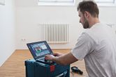 Pessoa a analisar dados de uma câmara térmica num computador portátil numa sala com um radiador.