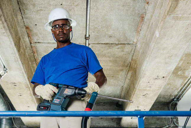 Pessoa que utiliza equipamento de segurança opera uma máquina de perfuração de impacto rotativa num estaleiro de obras.