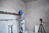 Uma pessoa que utiliza equipamento de segurança alinha azulejos de parede utilizando uma ferramenta de nivelamento a laser.
