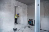 Uma pessoa que use equipamento de segurança marca uma parede guiada por uma ferramenta de nivelamento a laser verde.