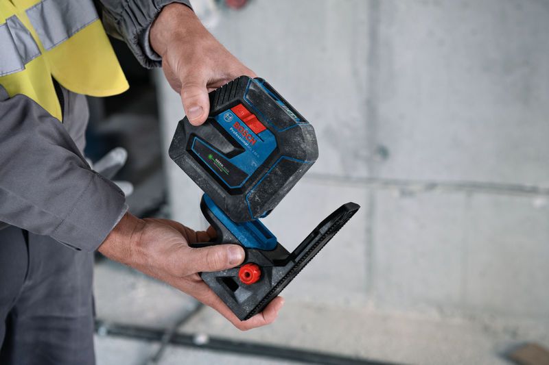 Uma pessoa que utiliza equipamento de segurança ajusta um acessório de ferramenta de nivelamento a laser em ambientes interiores.