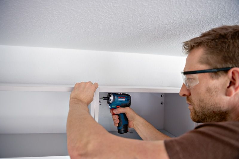 Uma pessoa que utiliza equipamento de segurança utiliza uma chave de fendas sem fios para montar um armário.