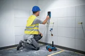 Uma pessoa que utiliza equipamento de segurança utiliza um scanner de parede numa parede de azulejos.