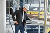 Uma pessoa que usa equipamento de segurança e um casaco aquecido inspeciona um tablet num estaleiro de obras.