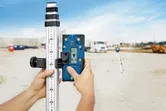 Uma pessoa ajusta um recetor laser numa mira de nivelamento num estaleiro de obras.