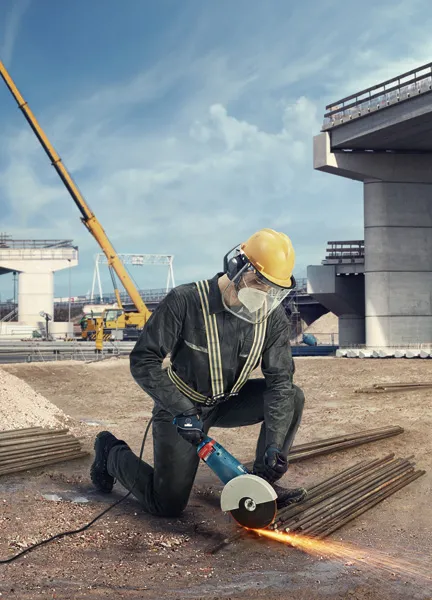 Uma pessoa que utiliza equipamento de segurança utiliza uma rebarbadora para cortar barras de metal num estaleiro de construção.