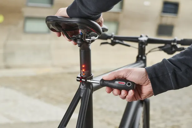 Pessoa a ajustar um espigão de selim de bicicleta com uma ferramenta de torque digital.