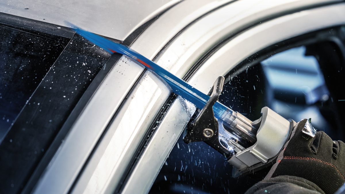 Uma pessoa que utiliza equipamento de segurança utiliza uma serra alternativa para cortar a estrutura de um automóvel.