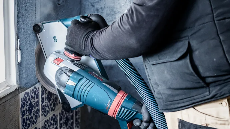 Uma pessoa que utilize equipamento de segurança opera uma retificadora de parede com extração de pó.