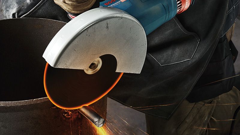 Uma pessoa que usa equipamento de segurança corta um tubo de metal com uma rebarbadora portátil.