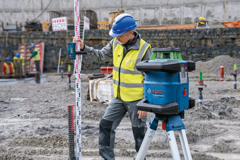 Operário que utiliza equipamento de segurança utiliza uma ferramenta de nivelamento a laser com um recetor a laser num estaleiro de construção.