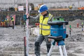 Operário que utiliza equipamento de segurança utiliza uma ferramenta de nivelamento a laser com um recetor a laser num estaleiro de construção.