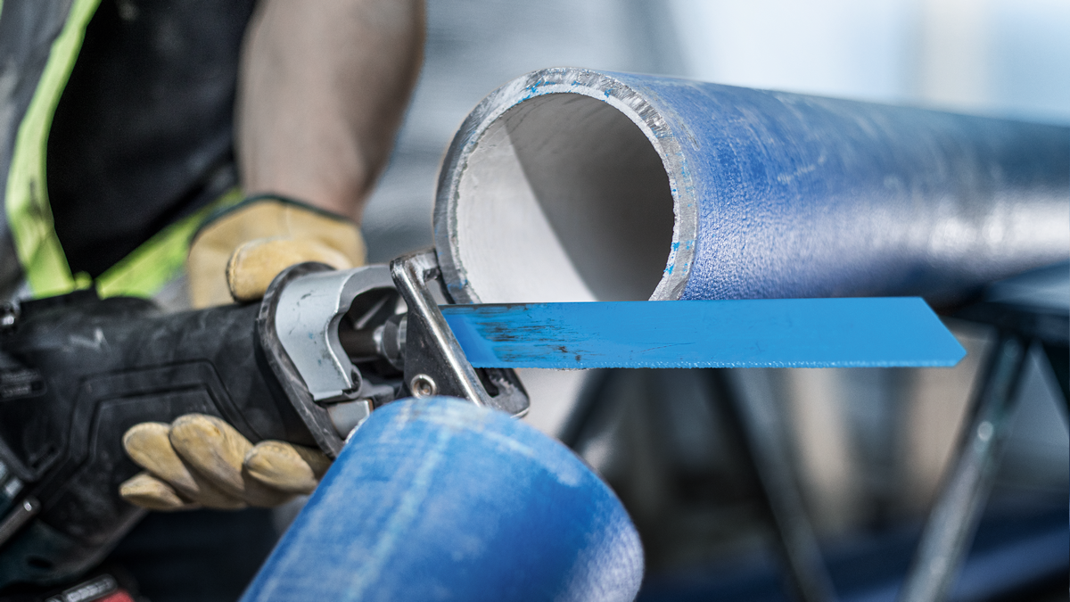 Uma pessoa que usa equipamento de segurança corta um tubo de ferro fundido azul com uma lâmina de serra recíproca.