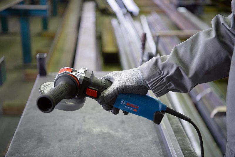 Uma pessoa que utilize equipamento de segurança segura uma rebarbadora perto de uma superfície metálica.