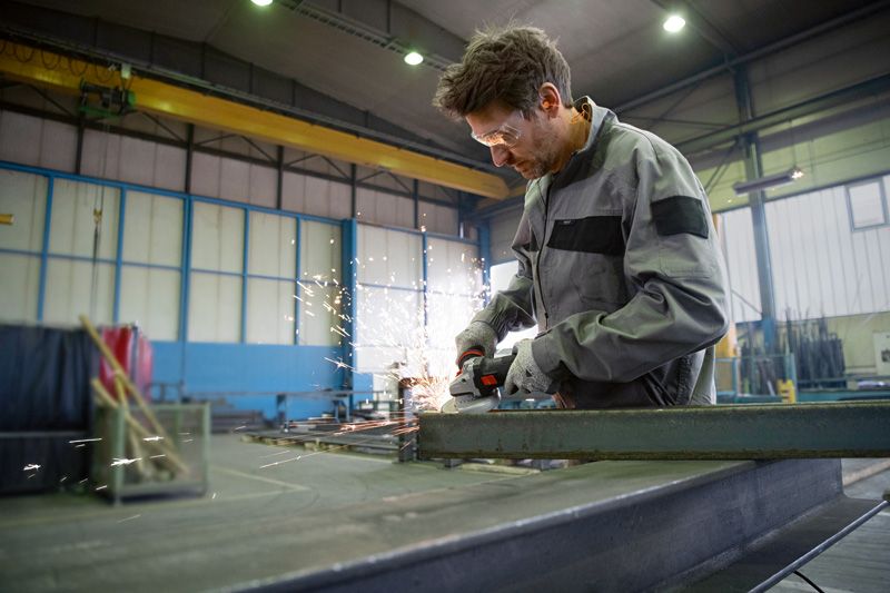 Uma pessoa que usa equipamento de segurança tritura metal com uma rebarbadora, e as faíscas voam.