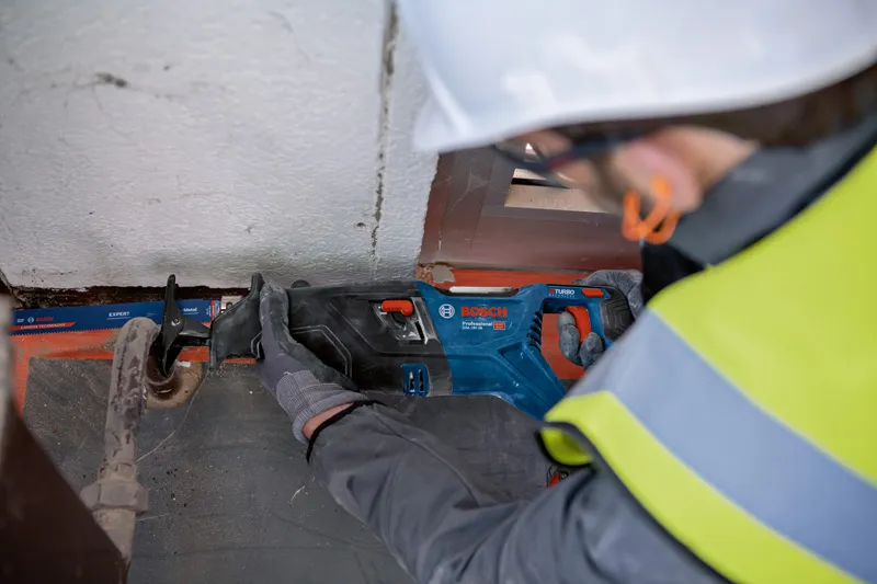 Uma pessoa que utilize equipamento de segurança utiliza uma serra alternativa para cortar um cano de metal.