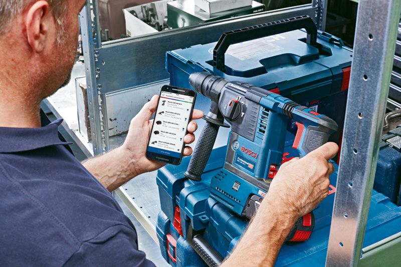 Pessoa que utiliza um smartphone para aceder a informações de manutenção de ferramentas perto de um berbequim elétrico.