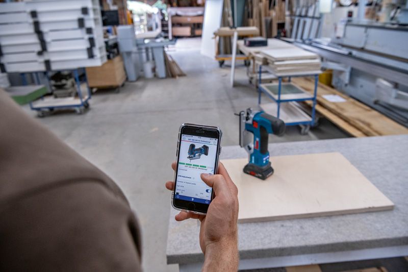 Uma pessoa utiliza um smartphone para consultar um berbequim sem fio numa marcenaria.