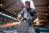 Uma pessoa que utiliza equipamento de segurança tritura um bloco de metal, produzindo faíscas numa fábrica.