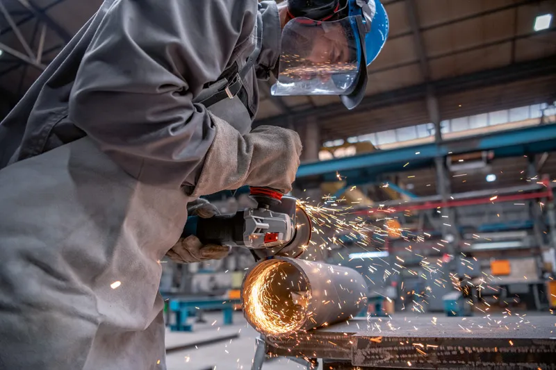 Uma pessoa que utiliza equipamento de segurança tritura um tubo de metal com uma rebarbadora.