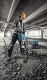 Uma pessoa que utiliza equipamento de segurança utiliza um martelo demolidor para demolir pavimento de betão.