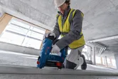 Uma pessoa que usa equipamento de segurança usa um pregador de betão sem fios num carril de metal.
