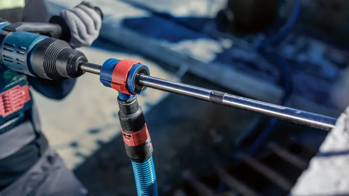 Uma pessoa que utiliza equipamento de segurança utiliza uma ferramenta rotativa para perfurar betão.