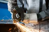 Uma pessoa que utiliza equipamento de segurança corta metal com uma rebarbadora, produzindo faíscas.