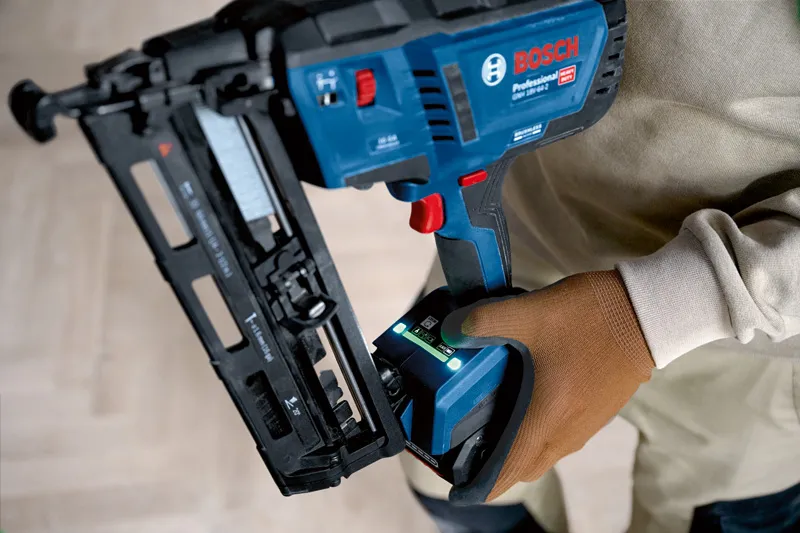 Uma pessoa que usa equipamento de segurança segura um prego de madeira sem fios num piso de madeira clara.