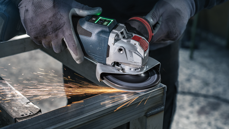 Uma pessoa que usa equipamento de segurança tritura metal, produzindo faíscas.