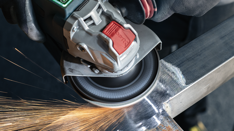 Uma pessoa que usa equipamento de segurança tritura metal, criando faíscas.