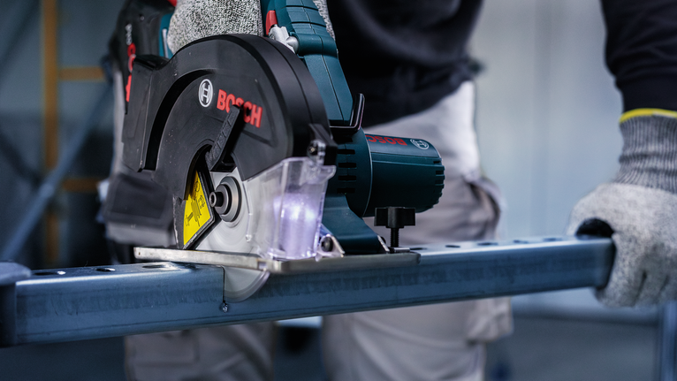 Uma pessoa que usa equipamento de segurança corta metal com uma serra circular.