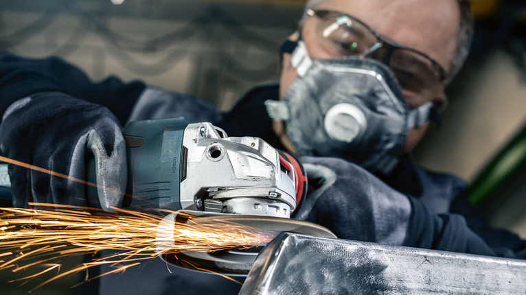 Uma pessoa que usa equipamento de segurança tritura metal, criando faíscas brilhantes.