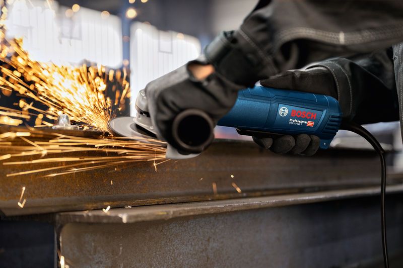 Uma pessoa que usa equipamento de segurança tritura metal, produzindo faíscas.