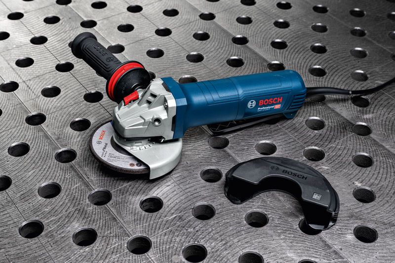 Rebarbadora angular com cabo lateral apoiada sobre uma bancada metálica com proteção de segurança amovível.