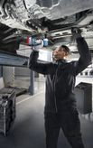 Uma pessoa que utiliza equipamento de segurança utiliza um berbequim elétrico para trabalhar debaixo de um veículo elevado.