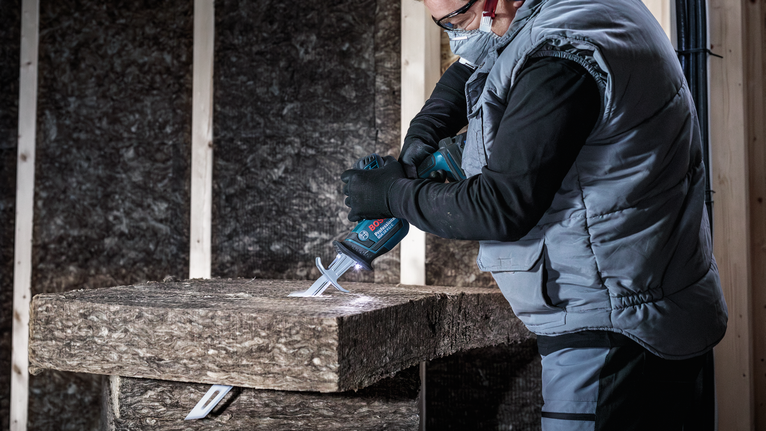 Uma pessoa que utilize equipamento de segurança corta material isolante com uma serra alternativa.