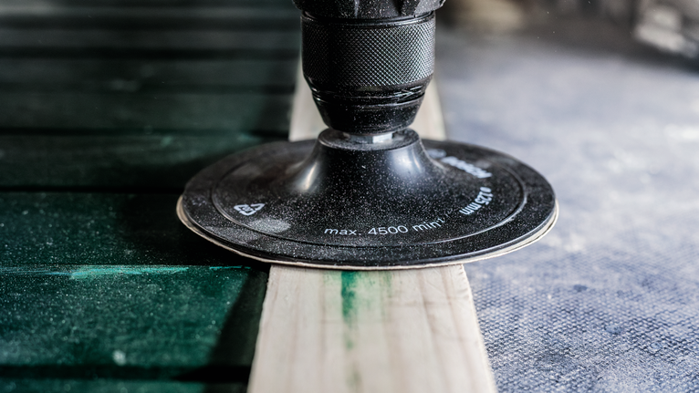 Uma lixadora rotativa alisa a superfície de uma tábua de madeira.