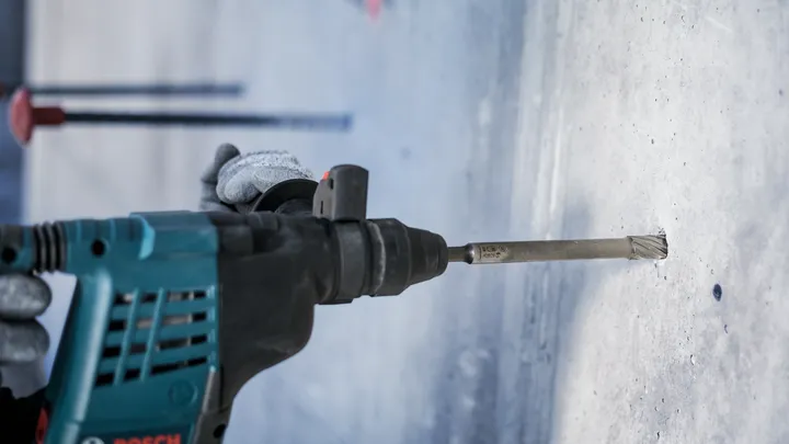Uma pessoa que utiliza equipamento de segurança perfura o betão com um martelo rotativo.
