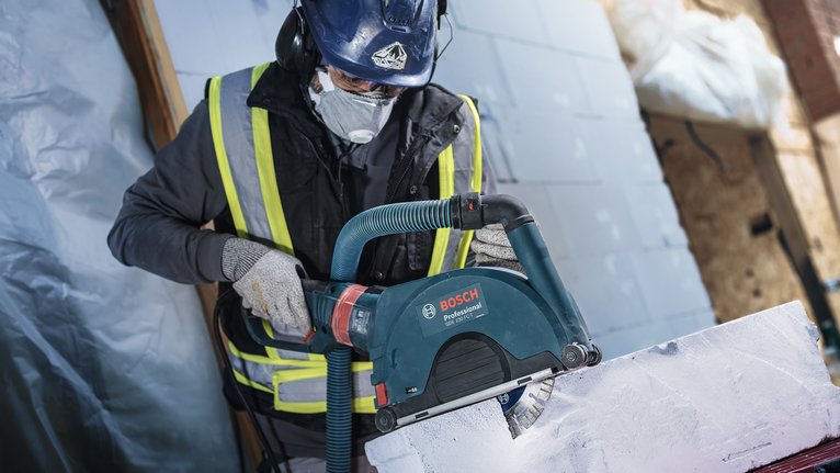 Trabalhador que usa equipamento de segurança corta um bloco de construção branco com uma serra elétrica.