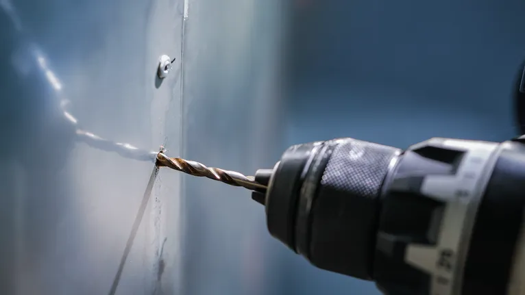 Uma máquina de perfuração elétrica faz um furo num painel de metal.