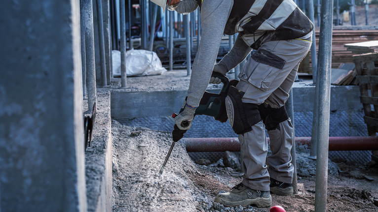 Uma pessoa que usa equipamento de segurança parte betão num canteiro de obras.