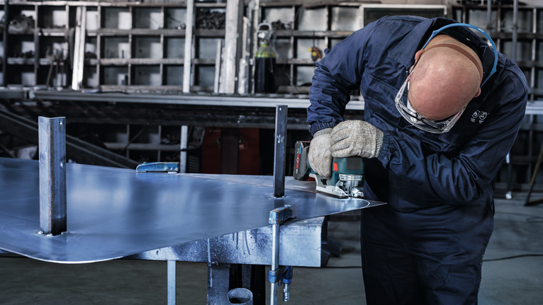 Uma pessoa que usa equipamento de segurança corta uma folha de metal com uma ferramenta elétrica.