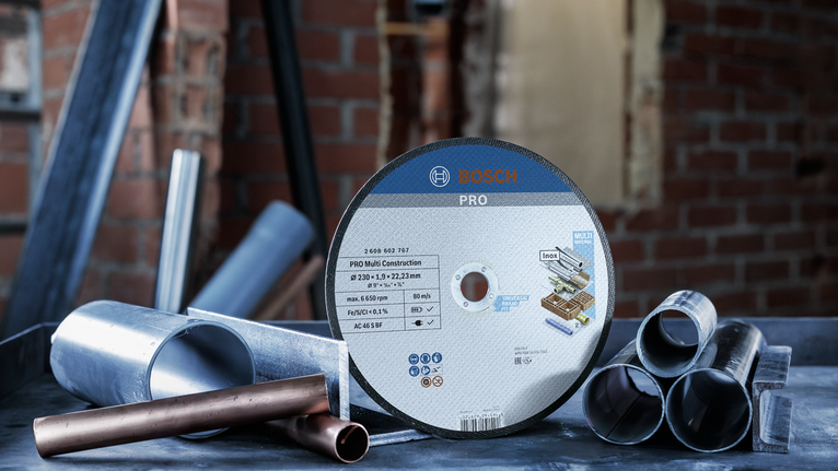 Um disco de corte de metal está sobre uma bancada de trabalho entre tubos de metal numa área de construção.