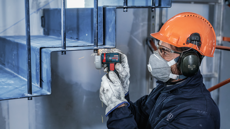 Uma pessoa que usa equipamento de segurança tritura uma escada de metal com uma ferramenta elétrica.