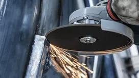 Uma pessoa que utiliza equipamento de segurança utiliza uma rebarbadora angular para cortar metal, gerando faíscas.